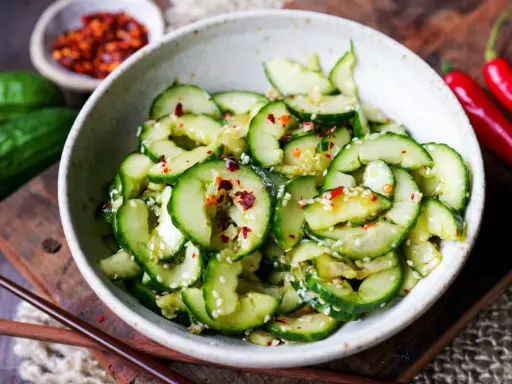 Erfrischender asiatischer Gurkensalat mit Sesam und Chili-Flocken, serviert in einer Schale mit Essstäbchen.