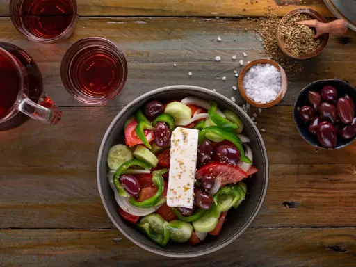 Frischer griechischer Salat mit Feta, Oliven, Tomaten, Gurken und Paprika, serviert mit Rotwein und Gewürzen.