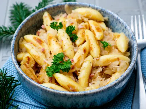Schupfnudeln mit Sauerkraut, garniert mit Petersilie, in einer blauen Schüssel. Ein Klassiker der deutschen Küche.