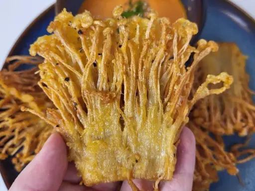 Knusprige Enoki Pilze, perfekt für ein einfaches enoki pilze rezept. Goldbraun frittiert und auf einem blauen Teller serviert.