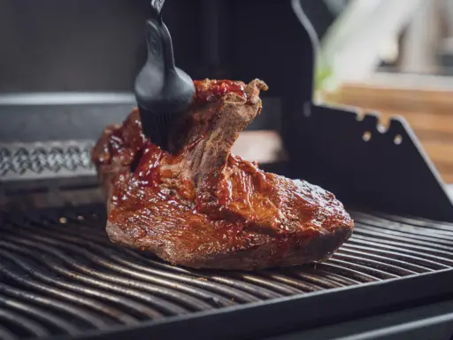Ein saftiges Brisket, sous vide gegart, wird mit einer BBQ-Sauce auf dem Grill glasiert.
