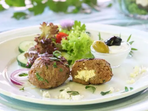 Gefüllte Bifteki mit Feta, serviert mit Salat, Gurken, Zwiebeln und Tzatziki. Ein köstliches Bifteki Rezept für Genießer.