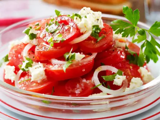 Frischer Tomatensalat mit Feta, Zwiebeln und Petersilie, garniert mit grobem Salz und Pfeffer. Ein leichter Genuss!