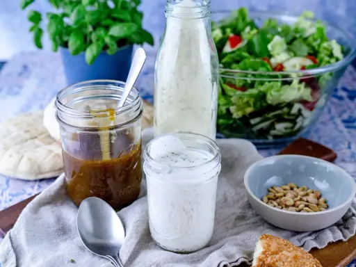 Ein Glas cremiges **ranch dressing** steht neben einem Glas mit brauner Soße, einem Salat und Brot.