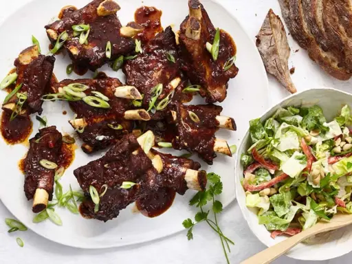 Saftige Spareribs mit BBQ-Sauce und Frühlingszwiebeln, serviert mit einem frischen Salat.