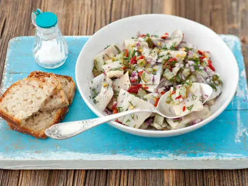 Frischer Matjessalat mit Gurke und Zwiebeln, garniert mit Dill, serviert mit Brot.