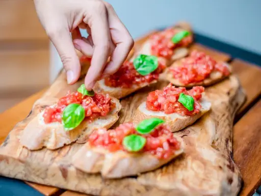Frische Bruschetta vom Grill, belegt mit Tomaten und Basilikum, wird von einer Hand garniert.