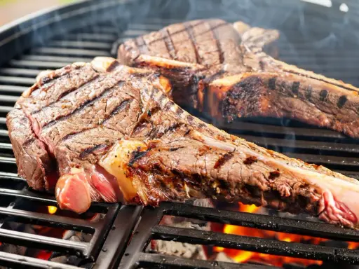 Zwei saftige tomahawk steaks brutzeln auf dem Grill. Rauch steigt auf, die Kohlen glühen.