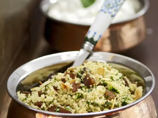 Ein köstlicher Couscous mit Rosinen, Mandelsplittern und frischer Petersilie, serviert in einer Kupferschale.