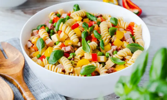 Bester Pasta Salat ohne Mayonnaise: Spiralnudeln mit Schinken, Erbsen, Paprika und Basilikum in einer weißen Schüssel.