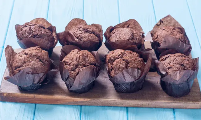 Acht schokoladige Muffins im braunen Papier auf einem Holzbrett. Perfekt für ein schokomuffins rezept.