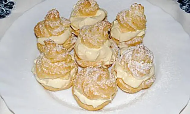 Windbeutel nach Omas Rezept, mit viel Sahne gefüllt und mit Puderzucker bestäubt, auf einem weißen Teller arrangiert.