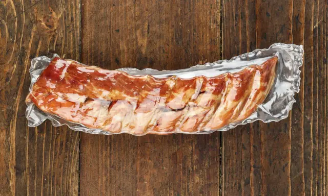 Vakuumverpackte Spareribs sous vide, bereit für die Zubereitung, liegen auf einer rustikalen Holzoberfläche.