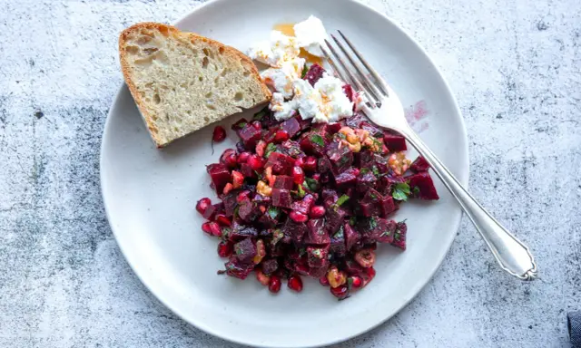 Ein bunter rote beete salat mit Granatapfelkernen, Nüssen und Ziegenkäse, serviert mit Brot.