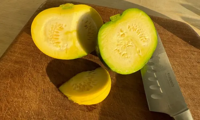 Zwei Hälften und ein Stück gelbe Zucchini liegen auf einem Holzbrett neben einem Messer.