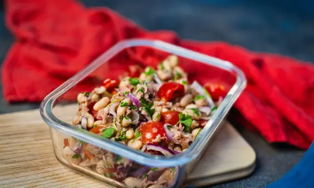 Frischer Thunfischsalat mit weißen Bohnen, Tomaten und roten Zwiebeln in einer Glasbox, bereit zum Mitnehmen.