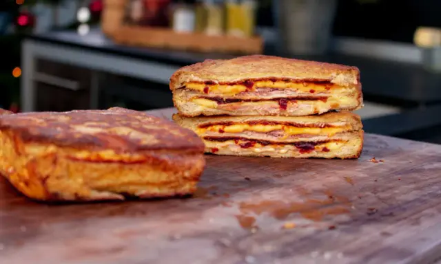 Zwei goldbraune Monte Cristo Sandwiches, gestapelt und mit Käse und Marmelade gefüllt, liegen auf einem Holzbrett.