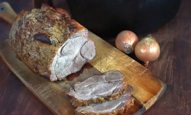 Saftiger Rinderbraten aus dem Dutch Oven, auf einem Holzbrett mit Zwiebeln.