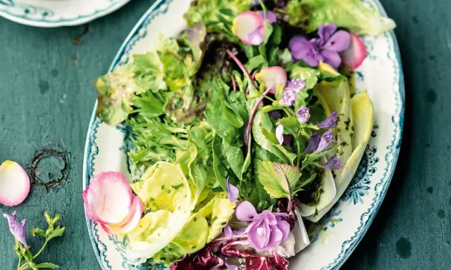 Ein bunter gemischter Salat mit zarten Blüten und Radieschen auf einem verzierten Teller.