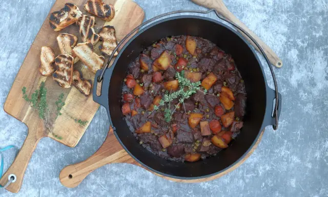 Herzhaftes Rindfleischgulasch im Dutch Oven, mit Kartoffeln, Karotten und Erbsen. Dazu geröstetes Brot. Perfekt für Dutch Oven Rezepte Rind.