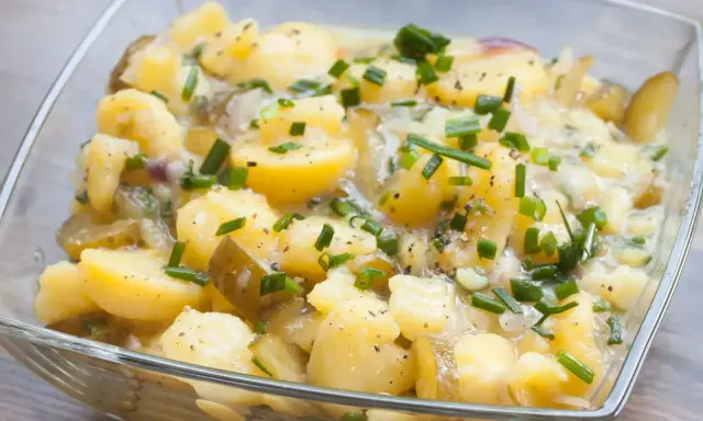 Kartoffelsalat ohne Mayo, mit Gurken, Zwiebeln und Schnittlauch in einer Glasschüssel.