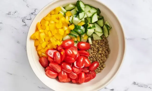 Zutaten für ein Linsensalat Rezept: gekochte Linsen, gewürfelte gelbe Paprika, Kirschtomaten und Gurkenstücke in einer Schüssel.