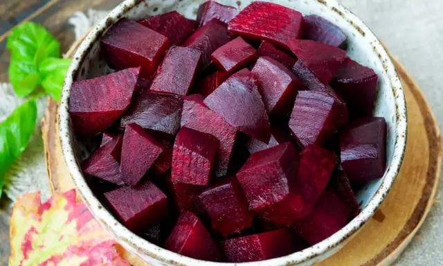 Schüssel mit gewürfelter roter Bete, bereit für die Kochzeit. Frische grüne Blätter und ein Herbstblatt liegen daneben.