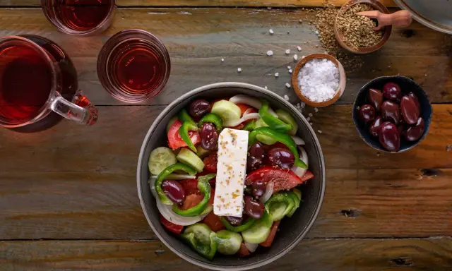 Frischer griechischer Salat mit Feta, Oliven, Tomaten, Gurken und Paprika, serviert mit Rotwein und Gewürzen.