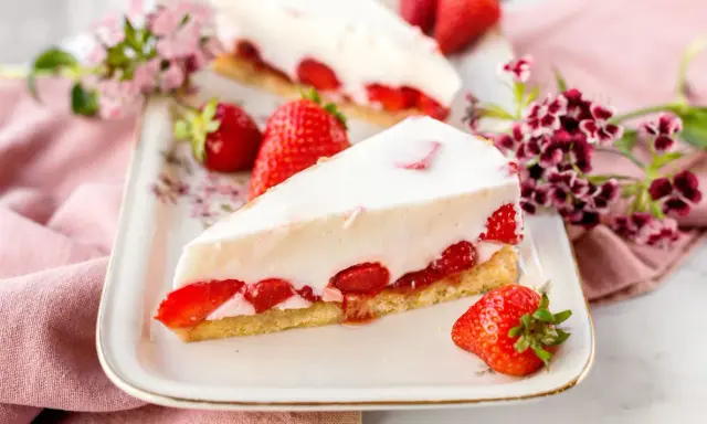 Ein Stück cremiger Erdbeerkuchen, der an Omas beste Kuchen Rezepte erinnert, mit frischen Erdbeeren und Blumen dekoriert.