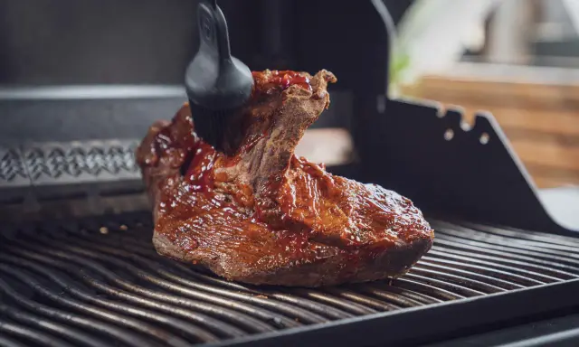 Ein saftiges Brisket, sous vide gegart, wird mit einer BBQ-Sauce auf dem Grill glasiert.