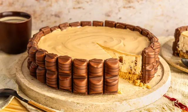 Eine köstliche Kinder Bueno Torte, umrandet von Schokoriegeln, mit einem Stück herausgeschnitten. Daneben eine Tasse Kaffee.