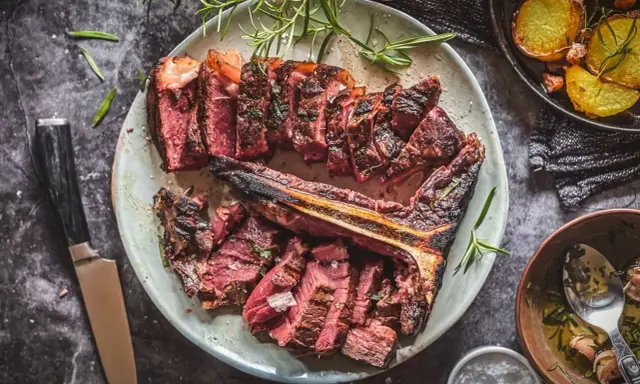 Saftiges, perfekt gegrilltes Bistecca alla Fiorentina, aufgeschnitten und mit Rosmarin garniert, daneben knusprige Kartoffeln.