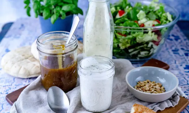 Ein Glas cremiges **ranch dressing** steht neben einem Glas mit brauner Soße, einem Salat und Brot.