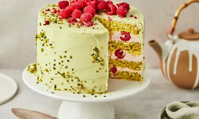 Himbeer Pistazien Torte mit frischen Beeren und knackigen Pistazien. Ein Stück ist angeschnitten und zeigt die saftige Füllung.