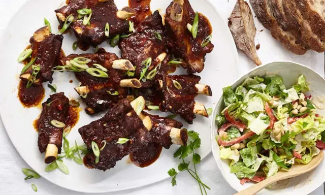 Saftige Spareribs mit BBQ-Sauce und Frühlingszwiebeln, serviert mit einem frischen Salat.
