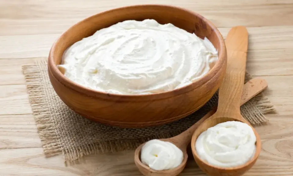 Cremiger Schmand in Holzschale und Löffeln. Ist Schmand gesund? Ja, in Maßen genossen, liefert er Kalzium und Proteine.