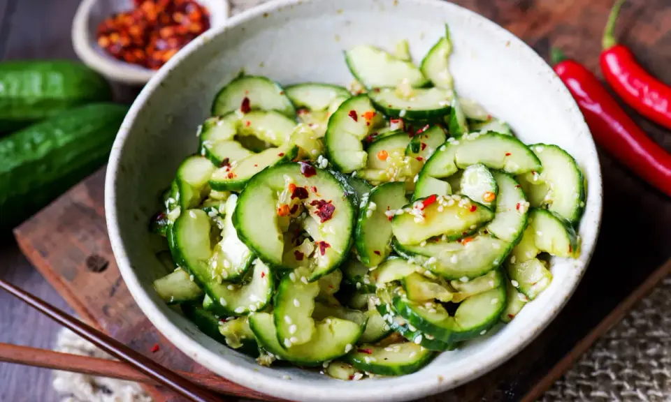 Erfrischender asiatischer Gurkensalat mit Sesam und Chili-Flocken, serviert in einer Schale mit Essstäbchen.