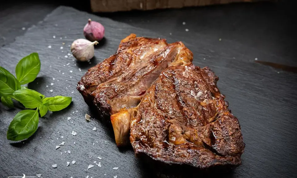 Perfekt gegrilltes Rib Eye Steak mit grobem Salz, Basilikum und Knoblauch auf schwarzem Stein.