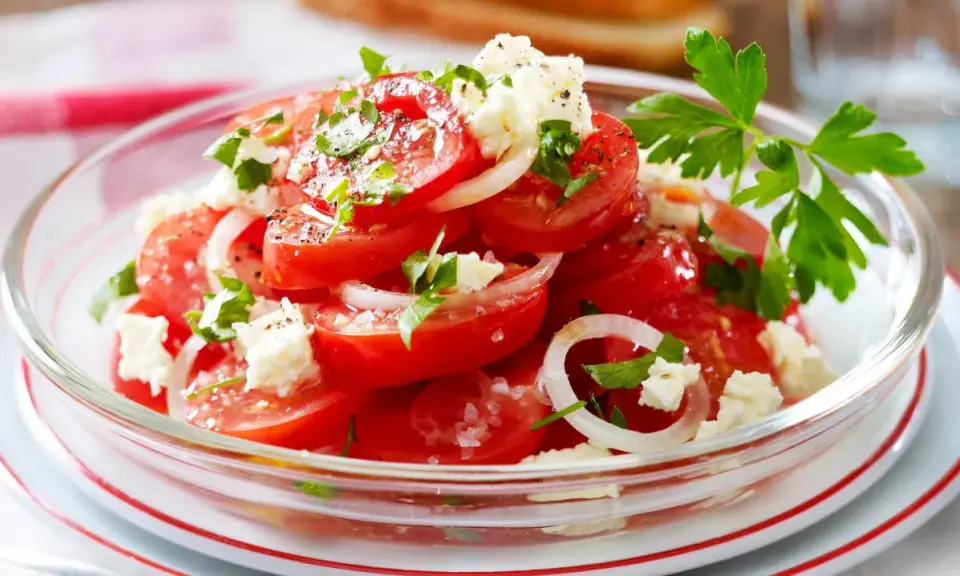 Frischer Tomatensalat mit Feta, Zwiebeln und Petersilie, garniert mit grobem Salz und Pfeffer. Ein leichter Genuss!