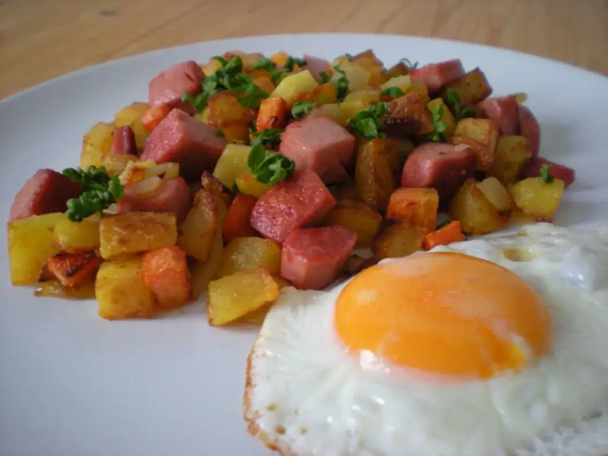 Pytt i panna: gebratene Kartoffelw&uuml;rfel, Wurstst&uuml;cke und ein Spiegelei auf einem Teller.