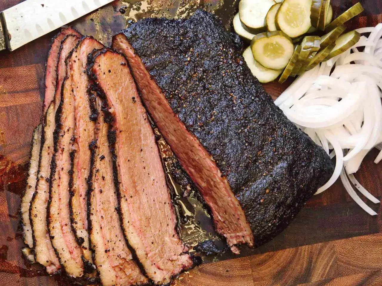 Perfekt gegarter Brisket Sous Vide, aufgeschnitten mit saftigen Scheiben, serviert mit Zwiebeln und Gurken.