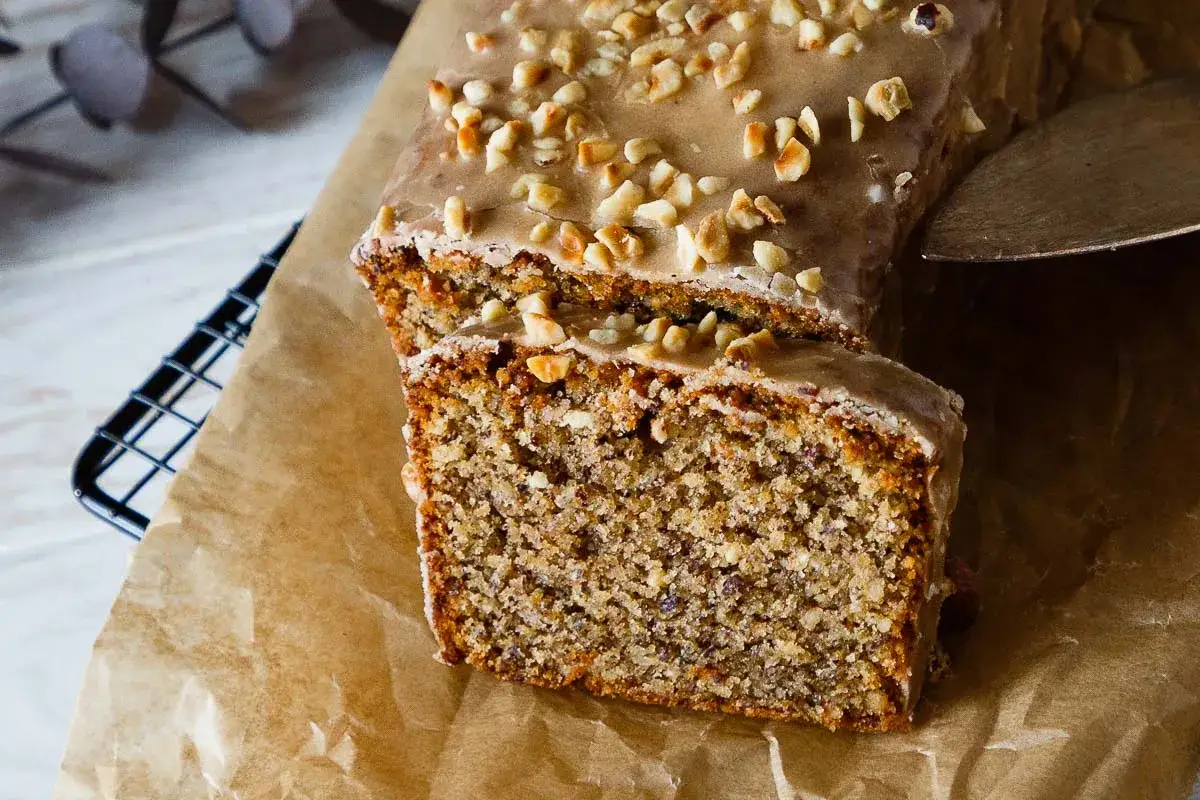 Omas Nusskuchen in Kastenform, mit Zuckerguss und gehackten N&uuml;ssen bestreut, wird auf Backpapier serviert.