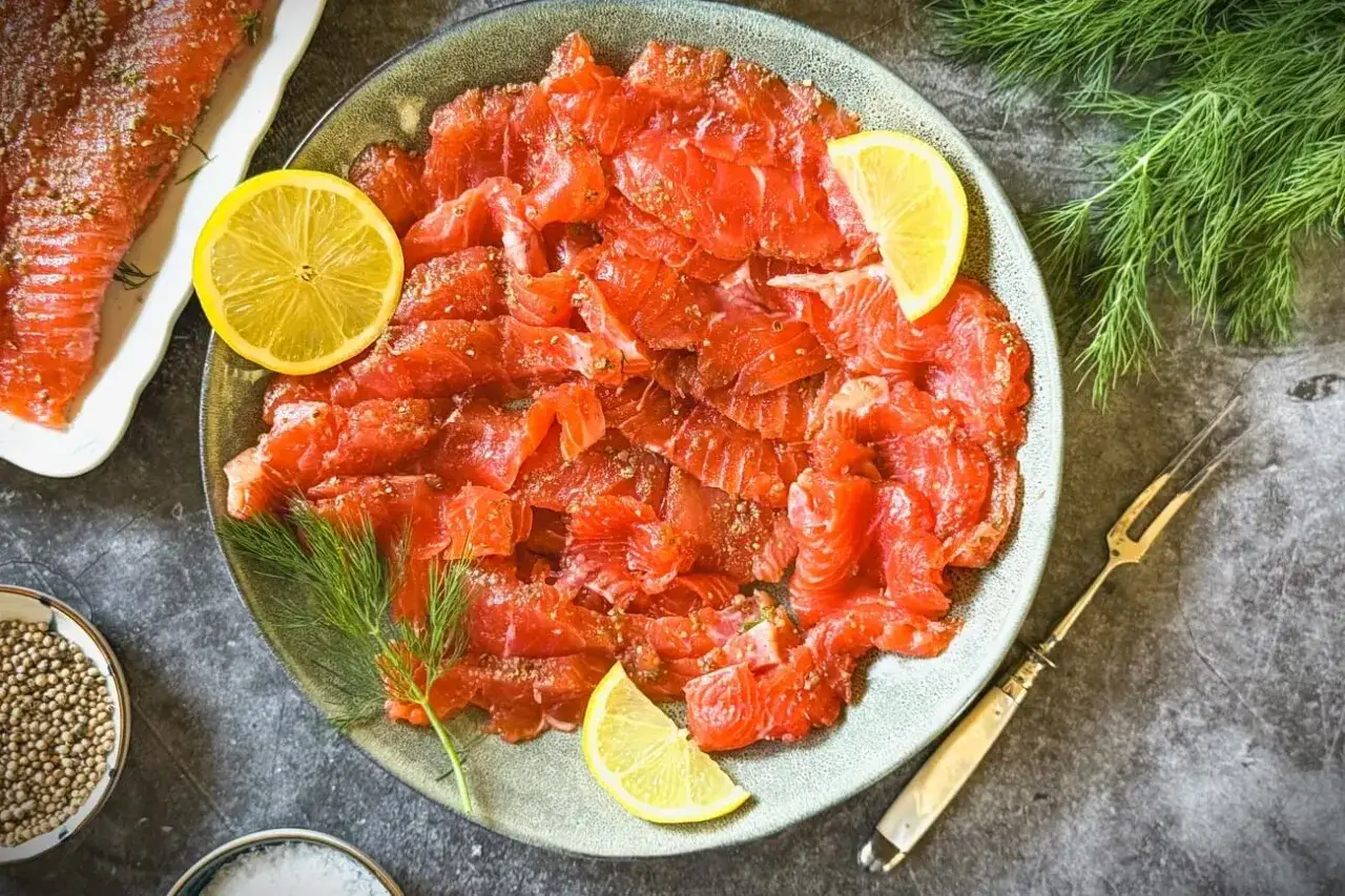 Frisch geschnittener Lachs, garniert mit Zitronenscheiben und Dill. Ein Blick auf die Zutaten zeigt, wie man Lachs beizt.