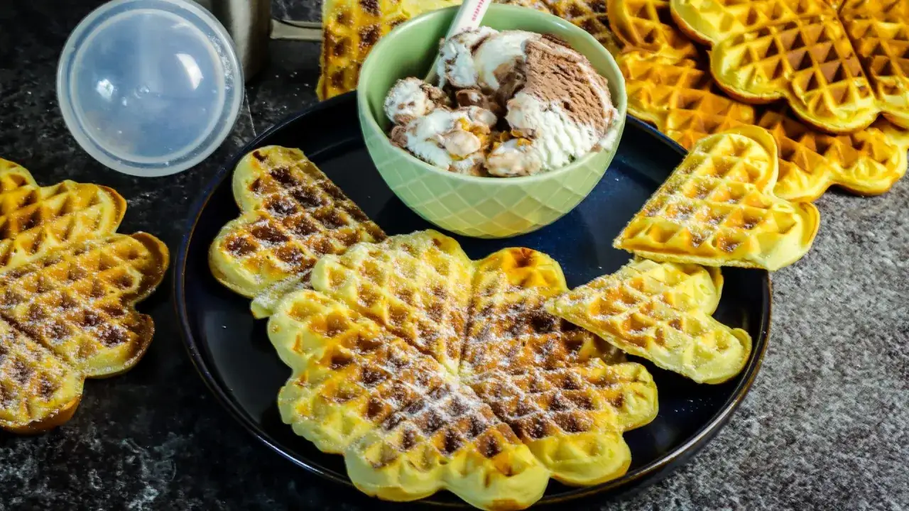 Herzf&ouml;rmige Waffeln ohne Ei, best&auml;ubt mit Puderzucker, serviert mit einer Sch&uuml;ssel Eiscreme. Ein Genuss f&uuml;r alle!