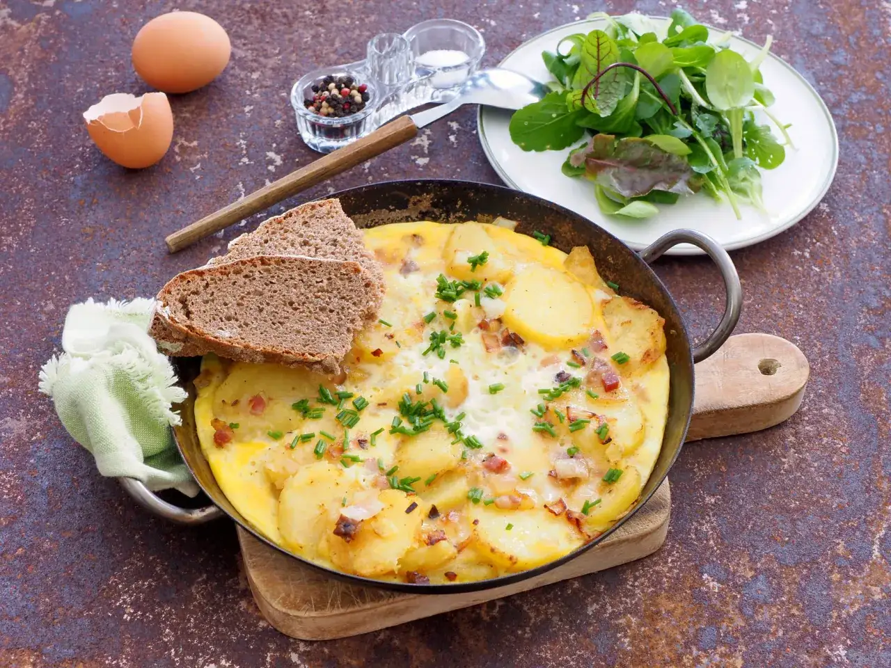 Herzhafte bauernpfanne mit kartoffeln und ei, garniert mit Schnittlauch. Dazu gibt es Brot und Salat.