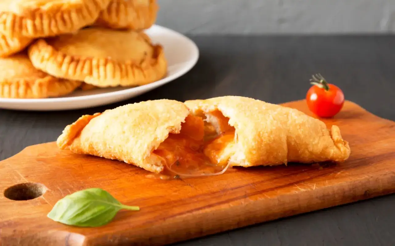 Leckeres Panzerotti-Rezept im Ofen: goldbraun gebackene Teigtaschen mit geschmolzener F&uuml;llung, garniert mit Basilikum und Kirschtomate.