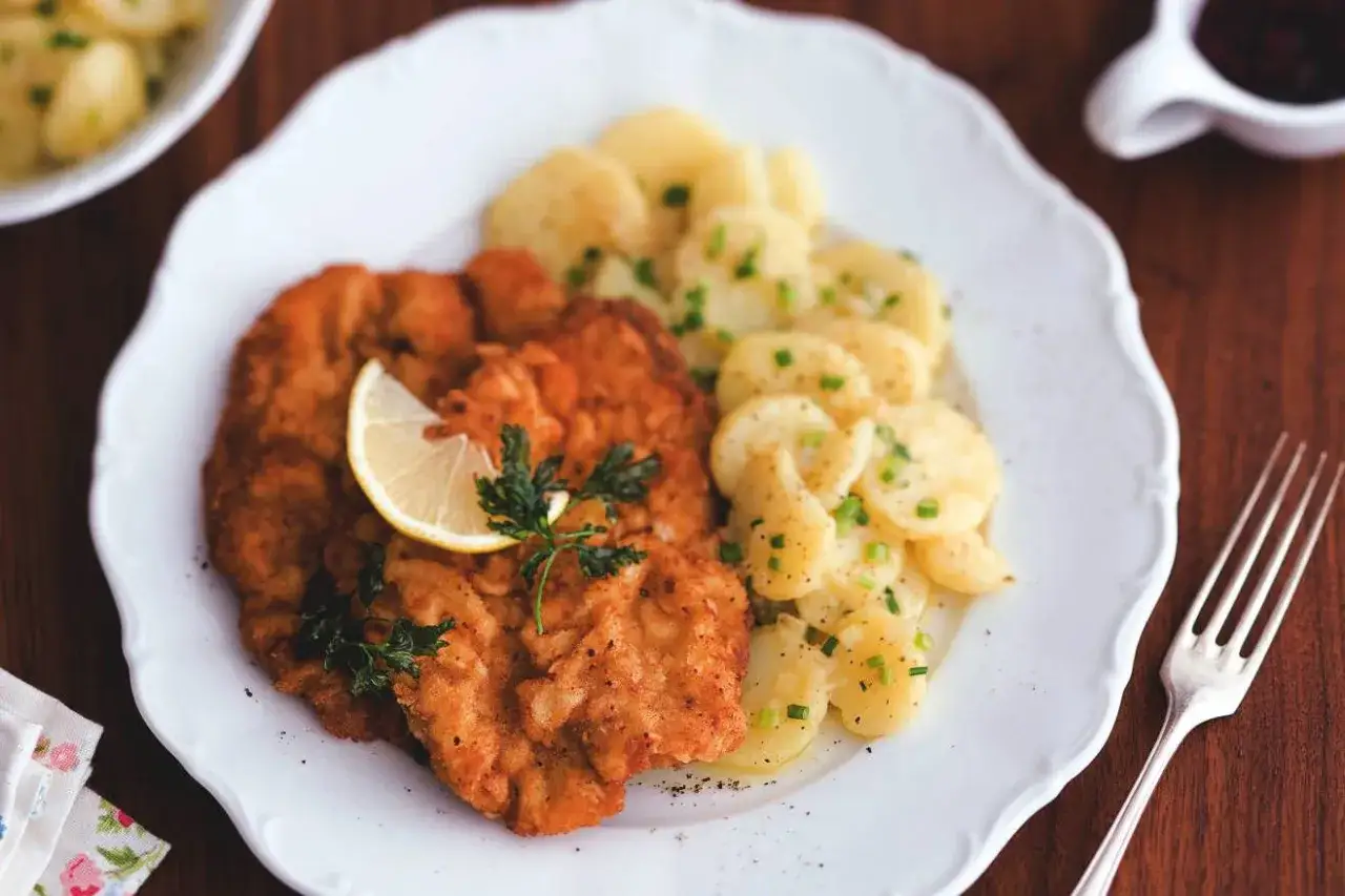 Ein knuspriges Wiener Schnitzel mit Kartoffelsalat und Preiselbeeren, garniert mit Zitrone und Petersilie.