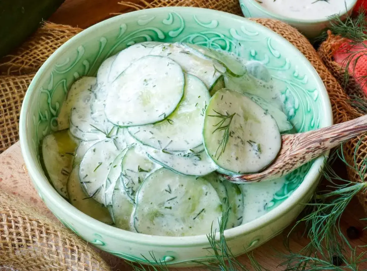 Frischer gurkensalat mit saurer sahne und dill, serviert in einer grünen schüssel.
