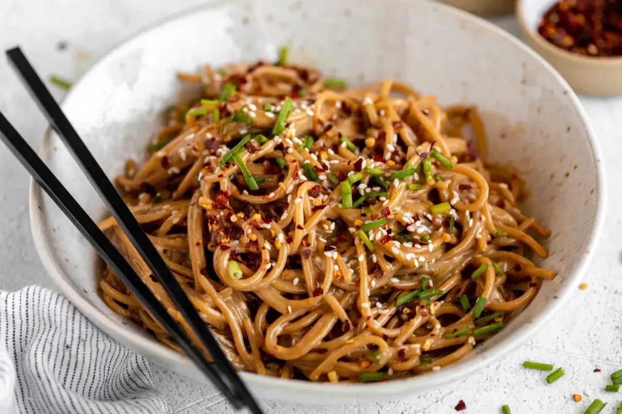 Schüssel mit Nudeln, garniert mit Sesam, Frühlingszwiebeln und Chiliflocken. Ist Sesam gesund? Ja, diese Nudeln sehen lecker und gesund aus!