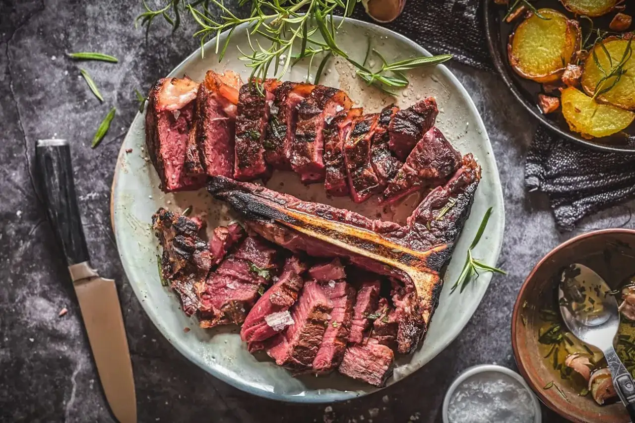 Saftiges, perfekt gegrilltes Bistecca alla Fiorentina, aufgeschnitten und mit Rosmarin garniert, daneben knusprige Kartoffeln.